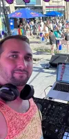 DJ Redline in front of his laptop and a crowd of people at a pride event